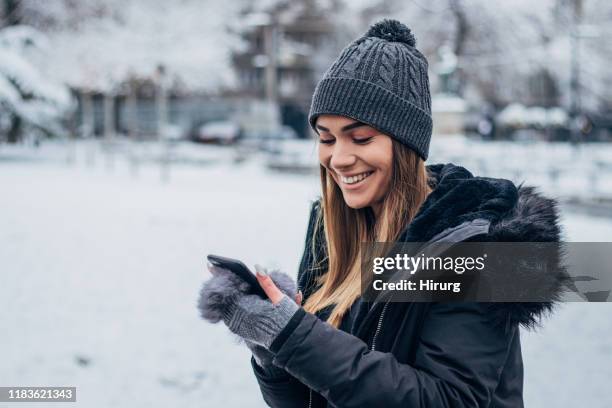 cheerful young woman text messaging - winter coat stock pictures, royalty-free photos & images
