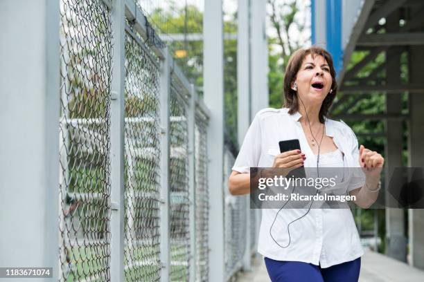 una anciana está usando su teléfono celular mientras hace ejercicio en el parque - mature latin women fotografías e imágenes de stock