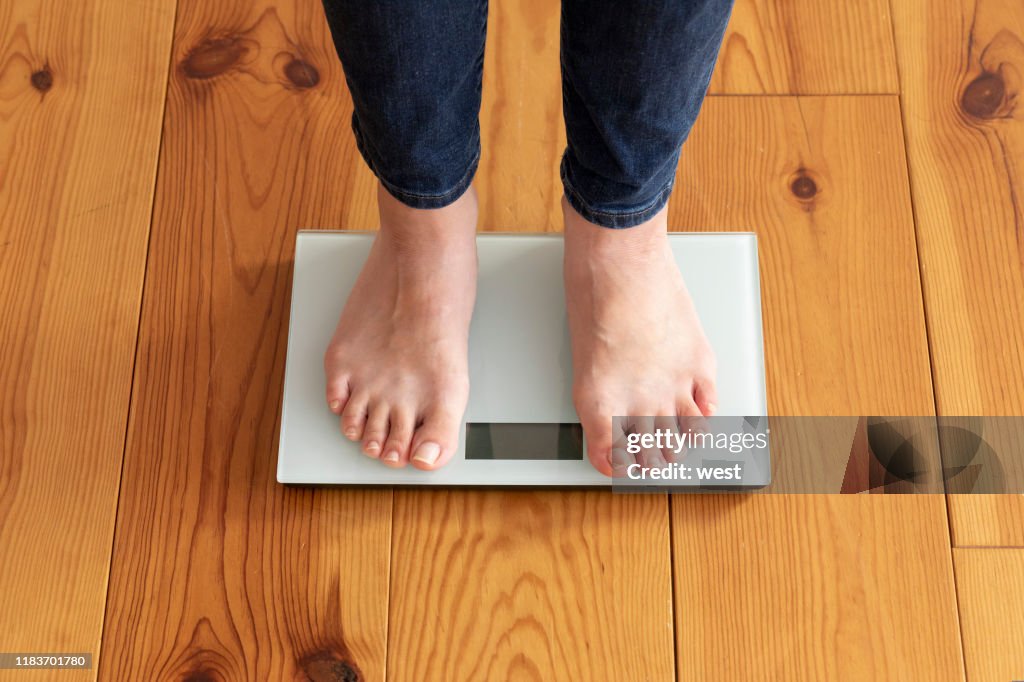 年輕女子的腳在木地板和重量秤