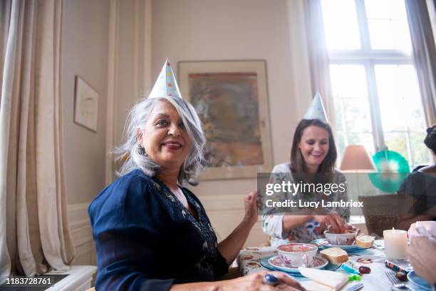 mixed group of women having fun with party hats at a birthday lunch party - older woman birthday stock pictures, royalty-free photos & images