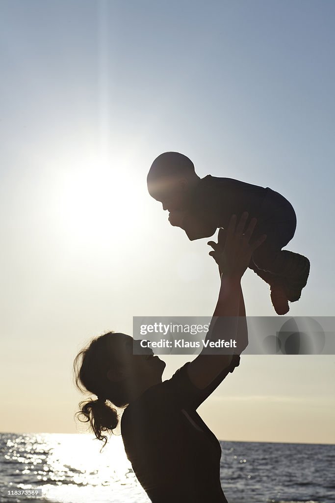 Mother lifting up baby boy on the beach