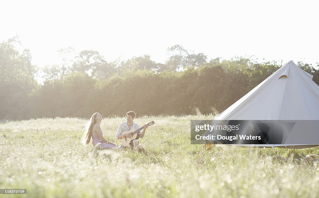 Couple camping in meadow playing music.