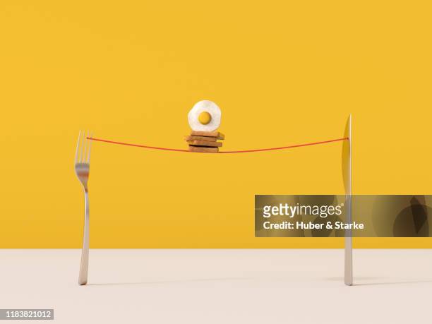slices of toasts and fried egg balance on cord taut between a fork and a knife