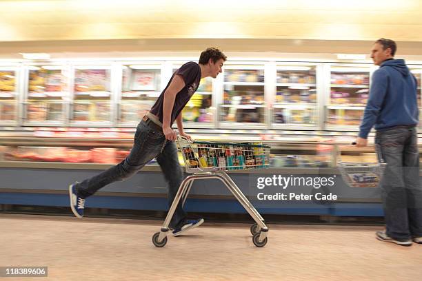 young man running in supermarket with trolly - shopping cart stock-fotos und bilder