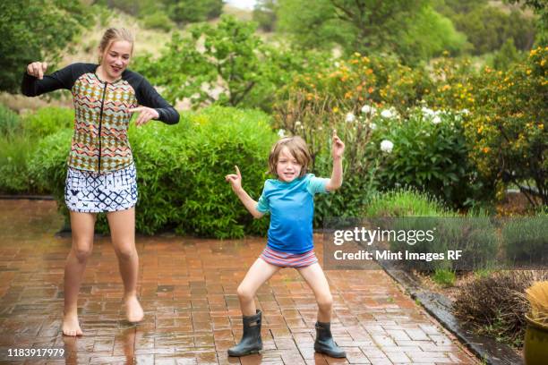 5 year old boy and his 13 year old sister dancing in the rain. - brother sister shower stock-fotos und bilder