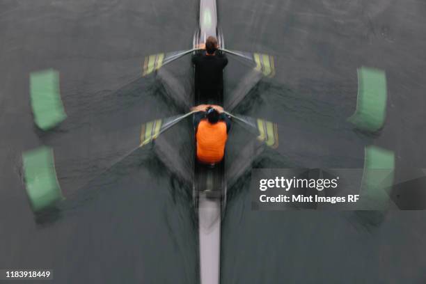 blurred motion overhead view of a double scull pairs boat, two oarsman in a sculling boat on the water, mid stroke. - boat rowing stock pictures, royalty-free photos & images