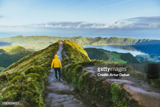 hiker with yellow raincoat in the viewpoint with volcanic crater in the azores islands. - san miguel portugal stockfoto's en -beelden