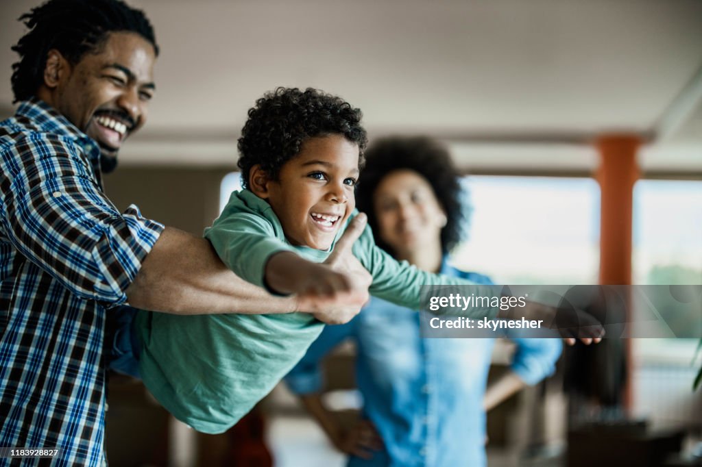 Feliz chico afroamericano divirtiéndose con su padre en casa.