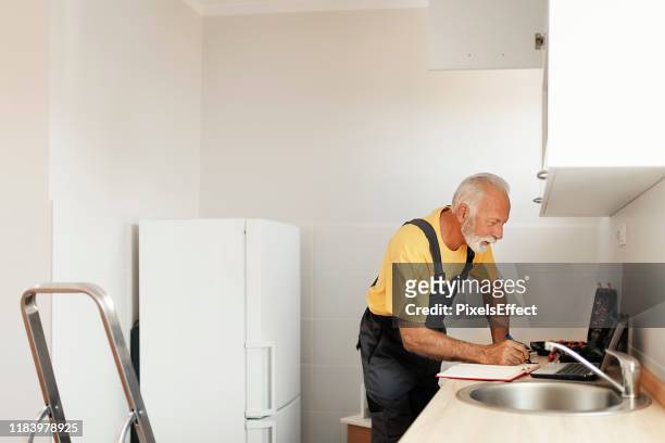 senior handyman fixing kitchen cabinet - kitchen straighten stock pictures, royalty-free photos & images