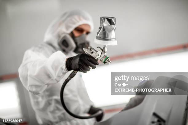 painting technician applying paint to a car bumper with a spray gun in a car painting booth of a body shop - spray booth stock pictures, royalty-free photos & images