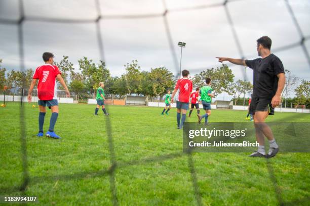 male coach directing young footballers during practice - junior stock pictures, royalty-free photos & images