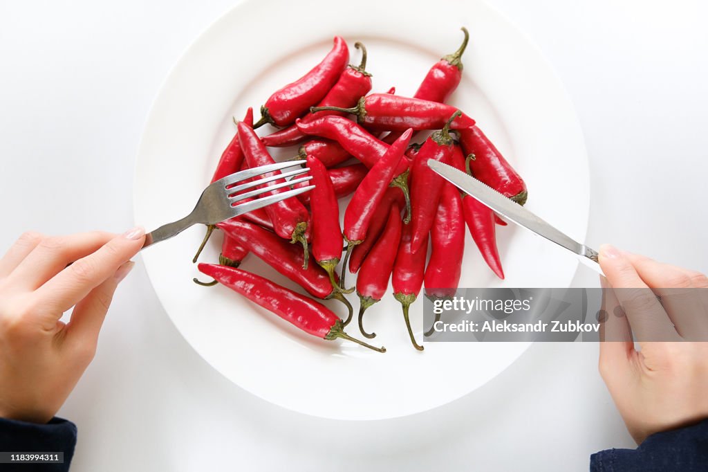 Girl hands with fork and knife, woman cuts red hot spicy Cayenne pepper on a white plate. Proper nutrition, vegetarian food, healthy lifestyle diet concept.