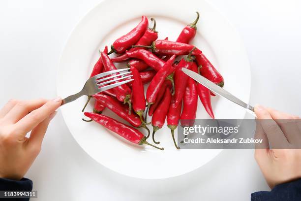 girl hands with fork and knife, woman cuts red hot spicy cayenne pepper on a white plate. proper nutrition, vegetarian food, healthy lifestyle diet concept. - eating spicy food stock pictures, royalty-free photos & images