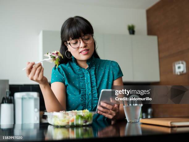 young businesswoman eating salad in lunch room and using phone - healthy working stock pictures, royalty-free photos & images