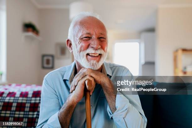 retrato de un hombre mayor feliz sentado y sosteniendo su bastón en un asilo de ancianos durante la mañana - hombre mayor fotografías e imágenes de stock