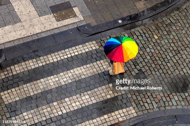 high angle view of cobbled street and person walking with multi-coloured umbrella - umbrellas from above stockfoto's en -beelden