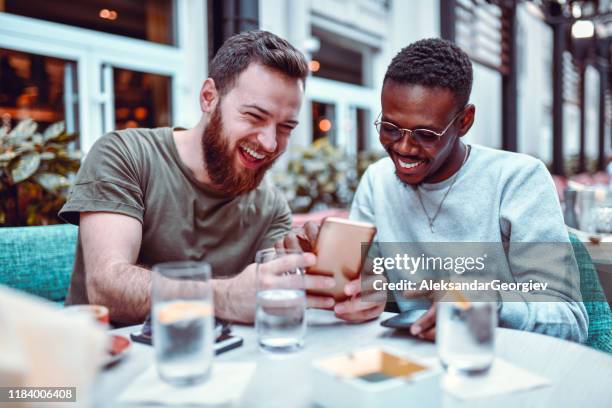 sueco masculino rindo enquanto navega mídia social com seu amigo africano - contar histórias - fotografias e filmes do acervo