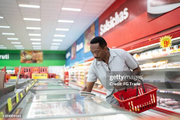 volwassen man op zoek en het kiezen van product in de supermarkt vriezer - frozen man stockfoto's en -beelden