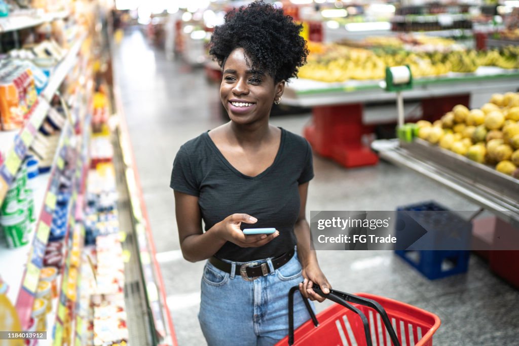 携帯電話を使用して、スーパーマーケットで製品を選択する��若い女性