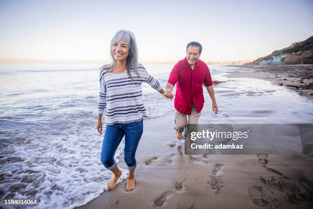 senior hispanic couple walking along the beach - liberty mutual insurance stock pictures, royalty-free photos & images