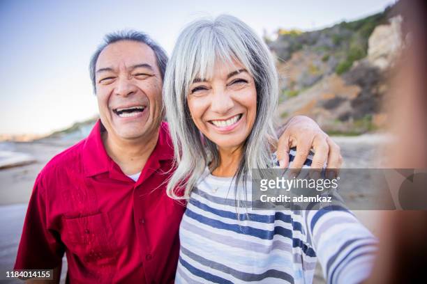 senior hispanic couple taking selfie at the beach - medicare stock pictures, royalty-free photos & images
