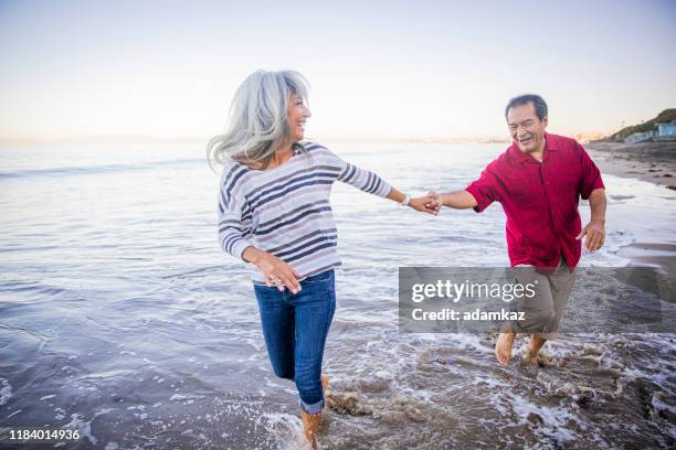coppia ispanica senior che cammina lungo la spiaggia - couple running on beach foto e immagini stock