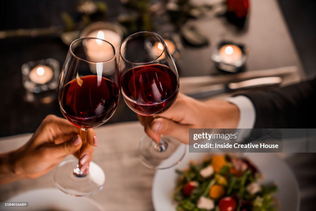 Close up of young couple toasting with glasses of red wine at restaurant