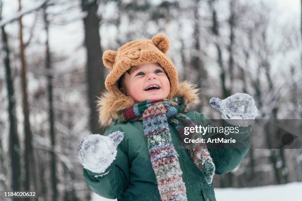 little toddler boy walking in the winter forest and having fun with snow enjoying winter outdoors. winter and lifestyle concept - mitten stock pictures, royalty-free photos & images