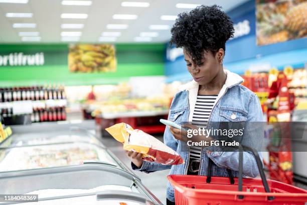 woman is shopping in supermarket and scanning barcode with smartphone - comprare stock pictures, royalty-free photos & images