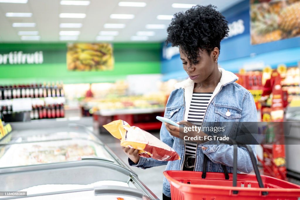 Kvinnan är shopping i Supermarket och scanning streckkod med smartphone