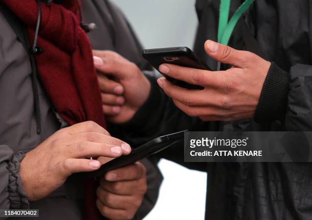 People hold smartphones in their hands while walking outside along a street in the Iranian capital Tehran on November 23, 2019. - Iranians have been...