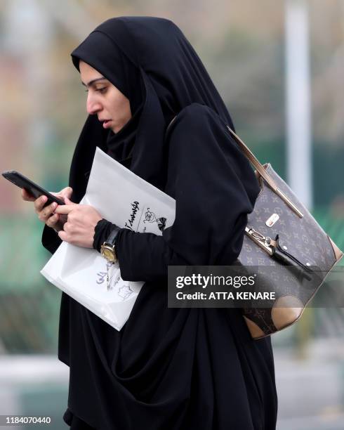 Woman uses a smartphone while standing along a street in the Iranian capital Tehran on November 23, 2019. - Iranians have been struggling to adjust...