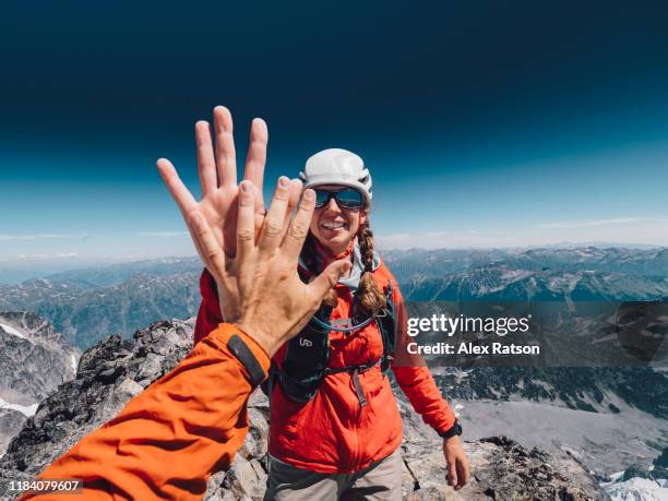 female mountain climber high fives her combing partner at the summit - summit stock pictures, royalty-free photos & images