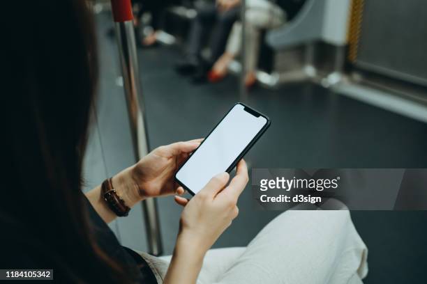 over the shoulder view of young woman using smartphone while riding on subway - crowded train station smartphone ストックフォトと画像