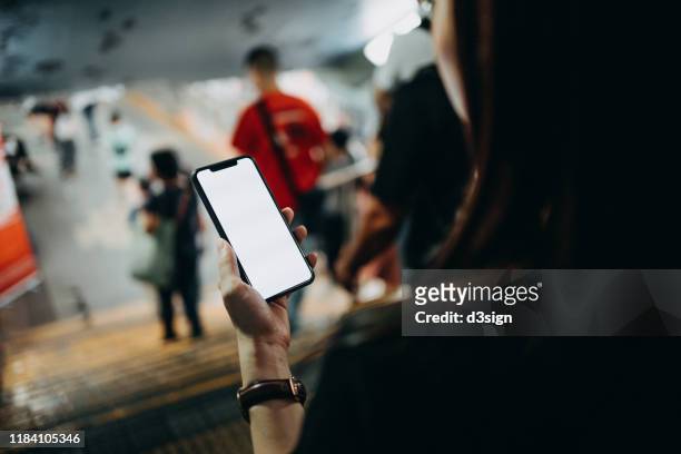 young woman using smartphone while commuting in the city as she walks pass a pedestrian tunnel - über die schulter stock-fotos und bilder