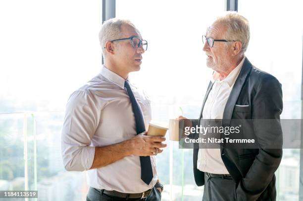 business people sharing great ideas concepts. senior business man holding cups of coffee and discussing something while sitting together near the window. - sharing coffee stockfoto's en -beelden