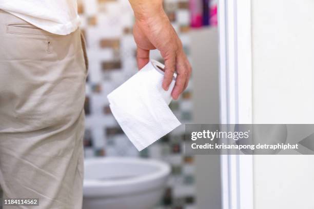man's hand, he holds a roll of toilet paper going to the bathroom toilet toilet background - diarrhoea foto e immagini stock