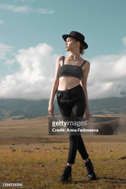 a young graceful girl dressed in a black hat with wide brim walks among the mountains. a clear sunny day in the altai mountains. a tourist trip to the depths of russian nature, high mountain ranges. - alta moda fotografías e imágenes de stock
