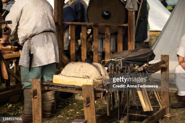 reconstruction of the forge. old crafts. craftsmen rest from work. blacksmith furs. metal tools. blacksmith forge. medieval historical role-playing games. dressed in an old outfit. bugle. - anna clarin fotografías e imágenes de stock