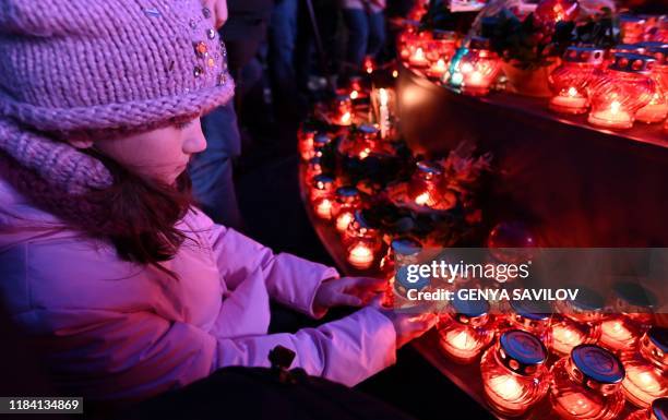 Child lights candle during a commemoration ceremony at a monument to victims of the Holodomor famine of 1932-33 in Kiev on November 23, 2019. -...