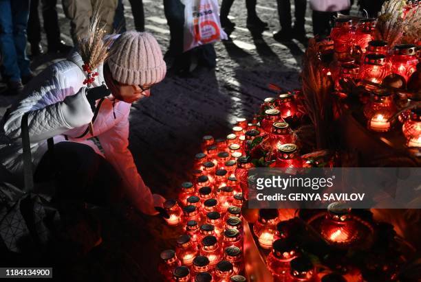 Woman lays symbolic sheave of wheat and lights candle during a commemoration ceremony at a monument to victims of the Holodomor famine of 1932-33 in...