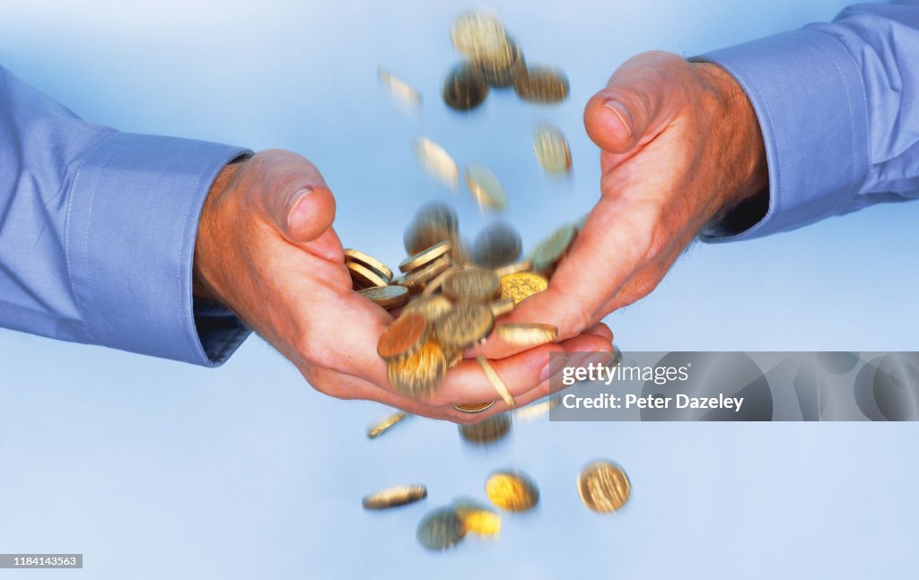 Gold coins falling through business man's hands