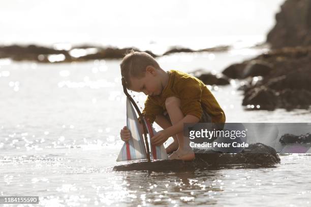 young boy playing with toy boat in the sea - spielzeugschiff stock-fotos und bilder