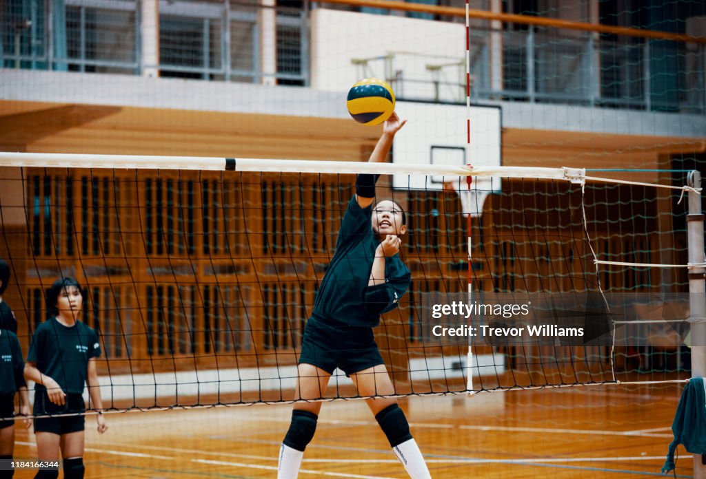 Young girl spiking the ball at a team volleyball practice in a school gym