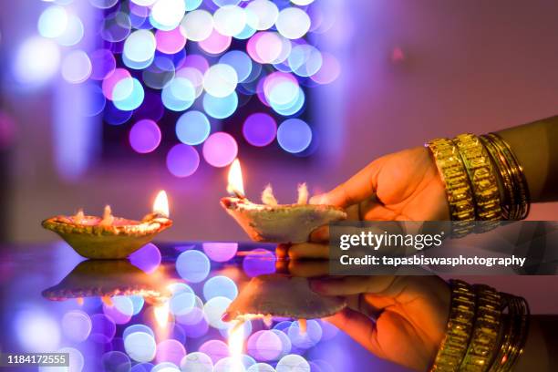 female hand holding a diwali lamp on the foreground of a beautifully illuminated background - diwali lights stock-fotos und bilder