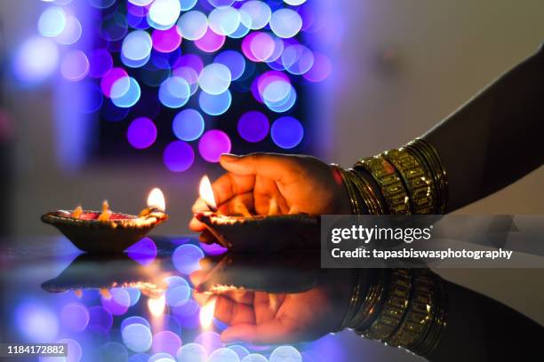 female hand holding a diwali lamp on the foreground of a beautifully illuminated background - diwali stock pictures, royalty-free photos & images
