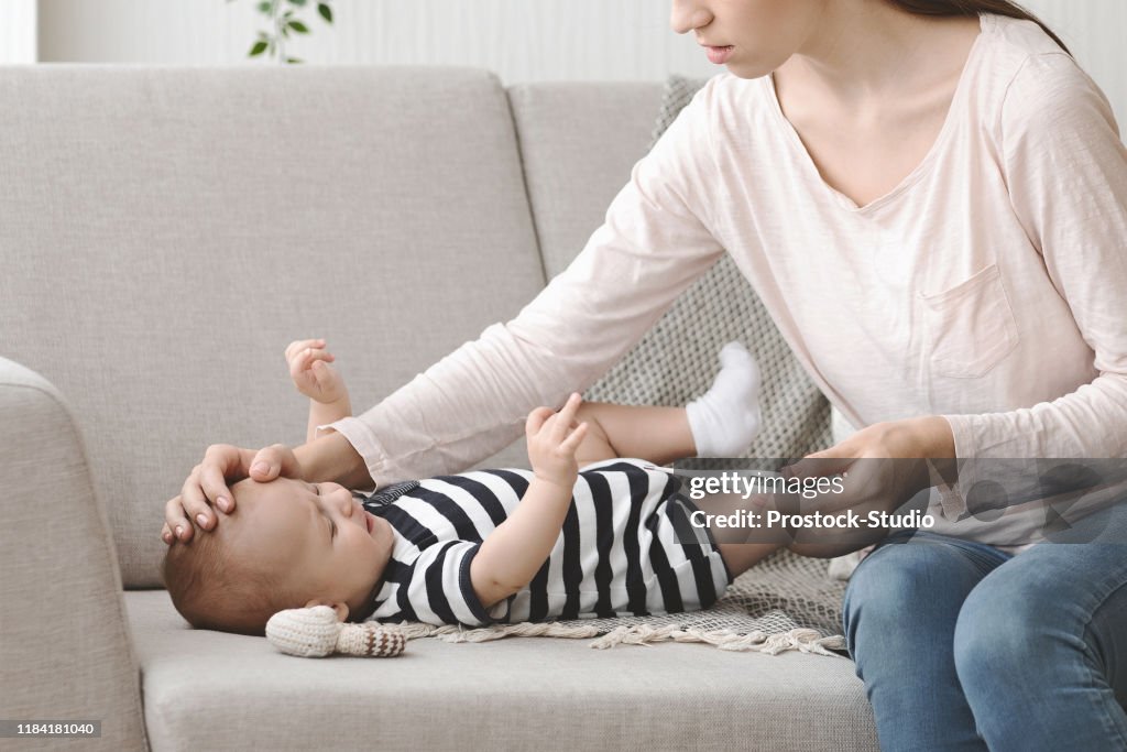 Mother holding thermometer and touching forehead of her ill baby