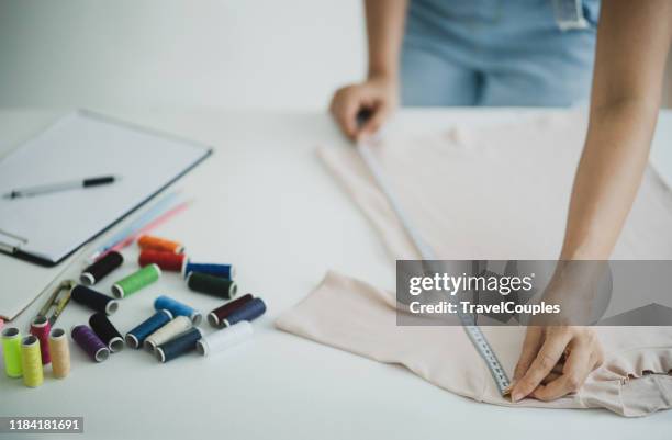 fashion designers working with fabric and clothing sketches at the studio full of tailoring tools and equipment. fashion designer cutting tailor made concept. female fashion designer hand working in home office workshop. - made to measure fashion stockfoto's en -beelden