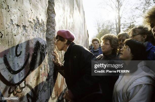 Parmi la foule une regarde à travers un trou creusé dans le Mur de Berlin après sa chute, le 12 novembre 1989, Allemagne.