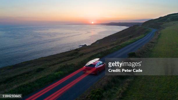 car driving along coastal road at sunset - landschaft rot stock-fotos und bilder
